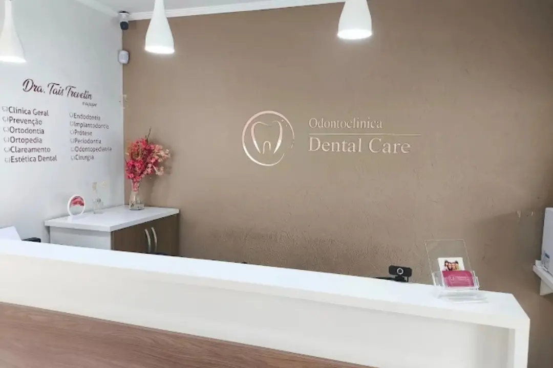 Balcão de atendimento e recepção da clínica Dental Care, com o logotipo destacado na parede e uma lista de especialidades odontológicas ao fundo.