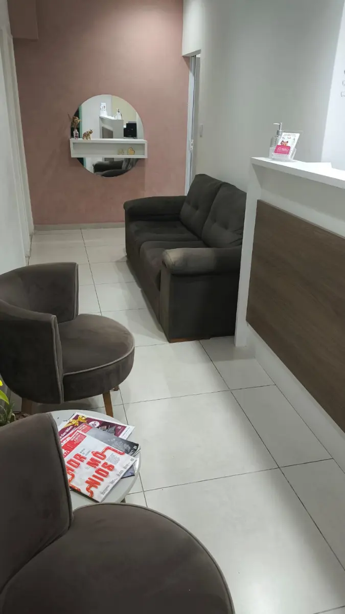 Sala de espera da clínica odontológica Dental Care em Vinhedo, contendo um sofá, poltronas, uma pequena mesa com revistas e um espelho decorativo na parede ao fundo.